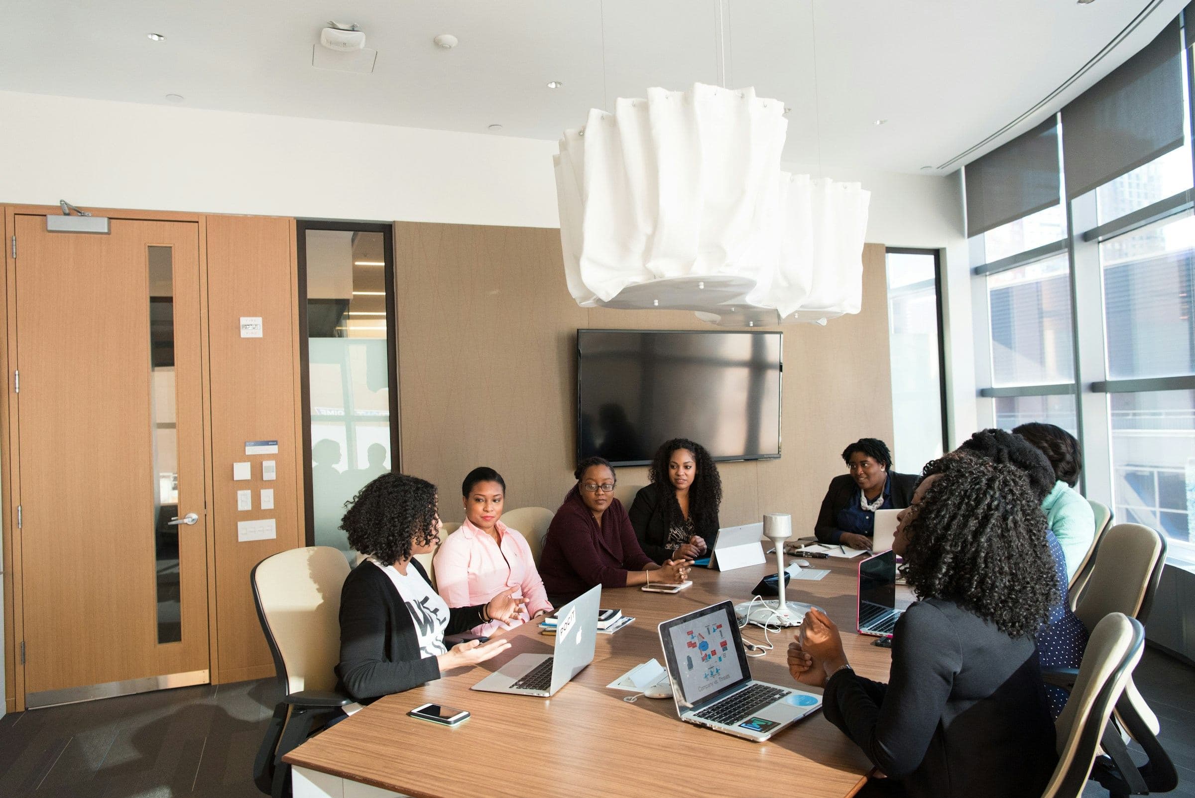 A team of colleagues talking around a meeting table with laptops open